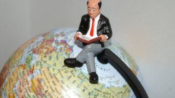 Ein Mann sitzt mit einem Buch auf einem Globus (Bild: Stephanie Hofschlaeger / pixelio.de)